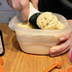 Hand scooping homemade vanilla ice cream out of a tub